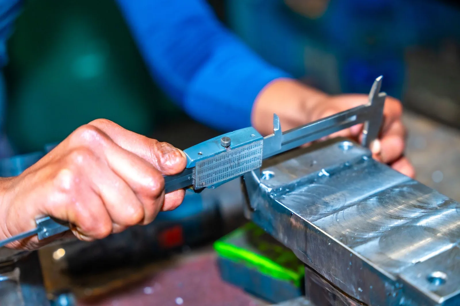 Un artisan mesure une pièce au pied à coulisse dans son atelier.